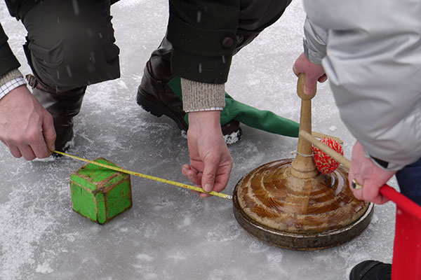 Zwei Leute messen den Abstand vom Eisstock zur Taube.