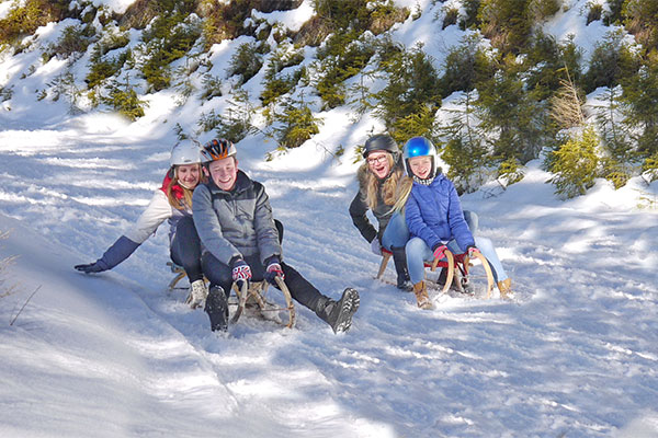 Leute fahren auf zwei Schlitten einen schneebedeckten Hang hinab.