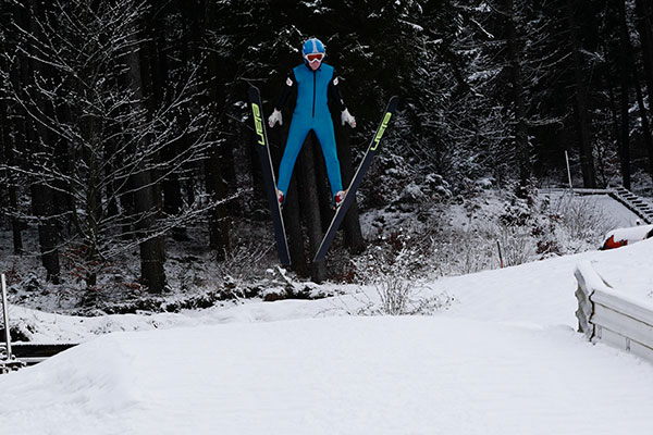 Ein Skispringer im blauen Anzug fliegt durch die Luft.